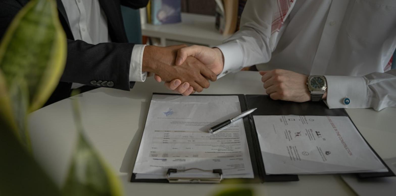 Dos personas se dan la mano sobre unos documentos contractuales, sellando un acuerdo