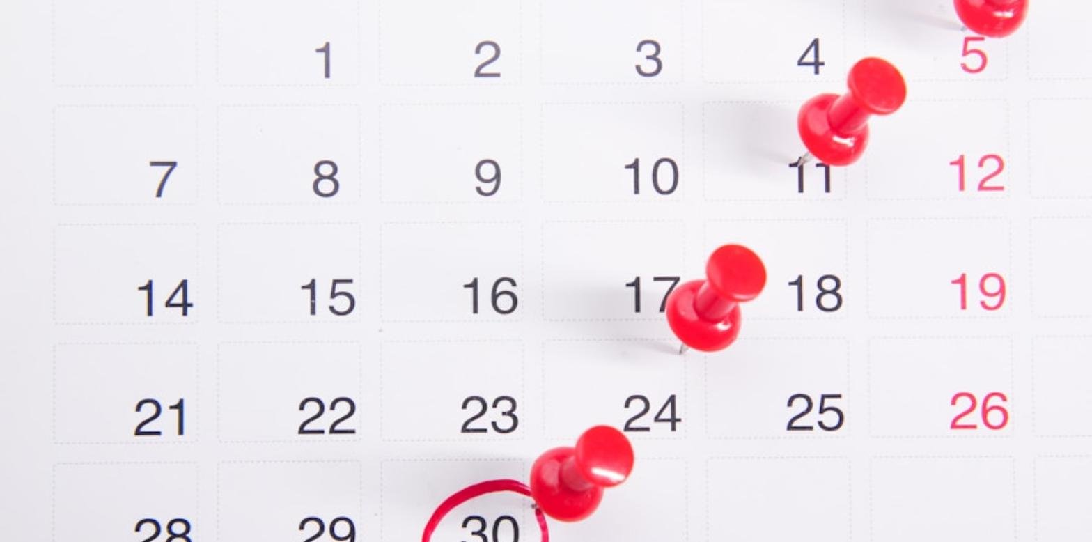 Calendario de pared con chinchetas rojas marcando varias fechas