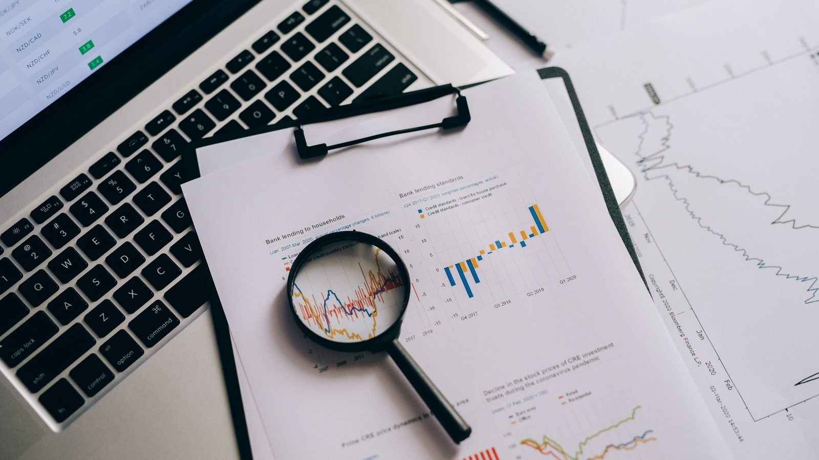 Lupa sobre gráficos e informes estadísticos junto a un portátil, simbolizando la vigilancia de datos