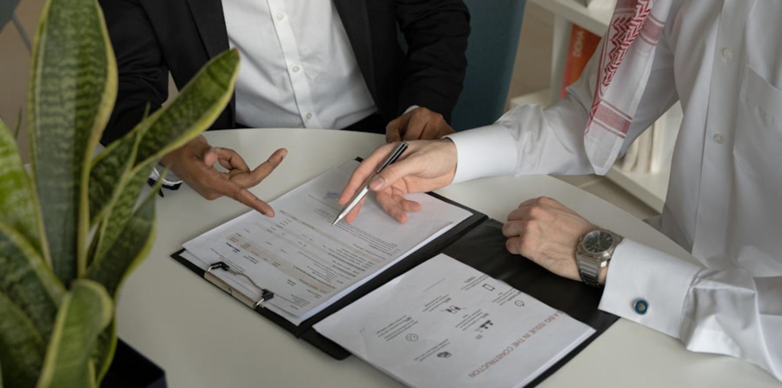 Dos personas revisando y señalando un documento sobre una carpeta en una mesa de oficina